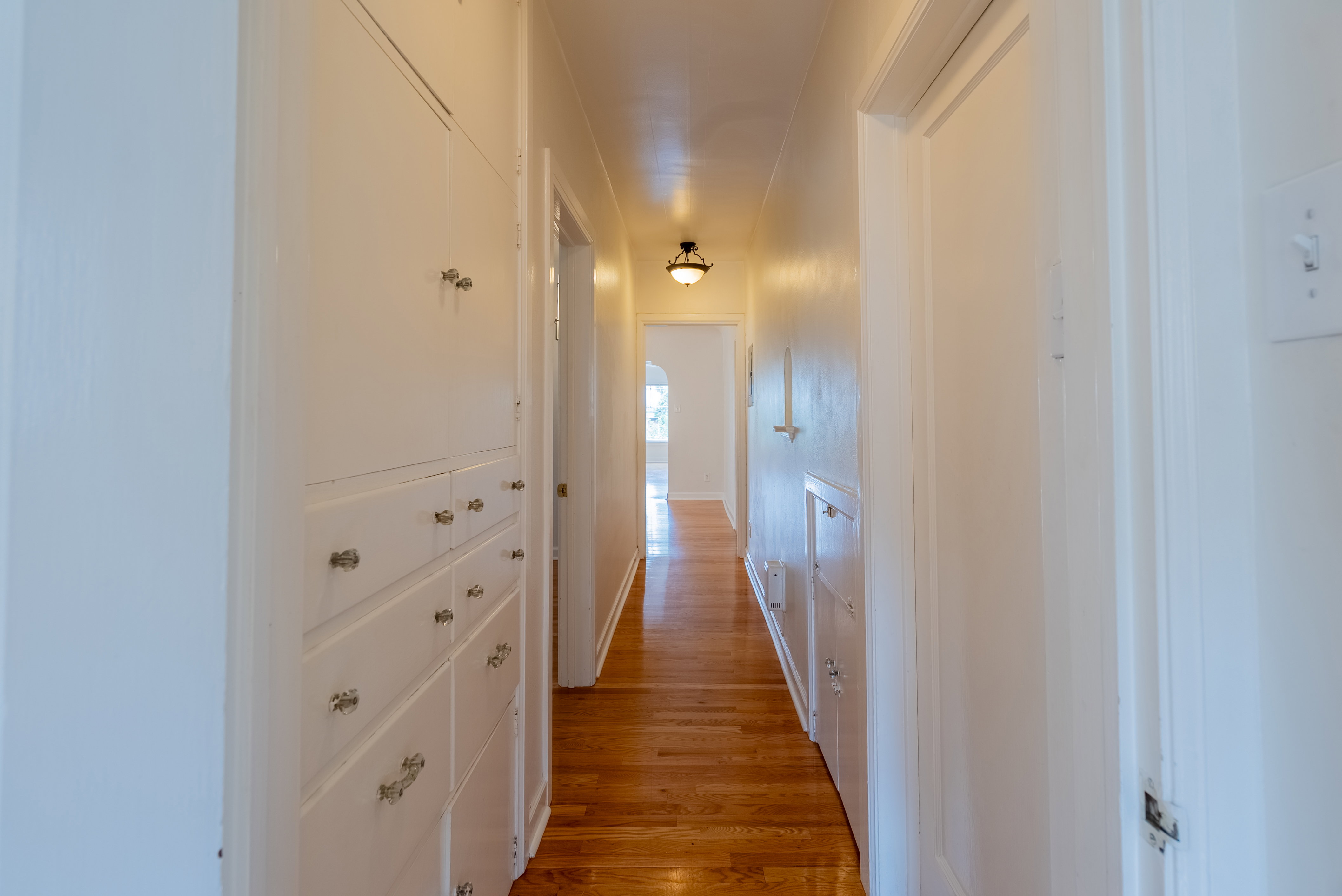 Hallway featuring built-in cabinetry with paneled doors and drawers, wood-finish flooring, a flush-mount ceiling light fixture, and white painted walls