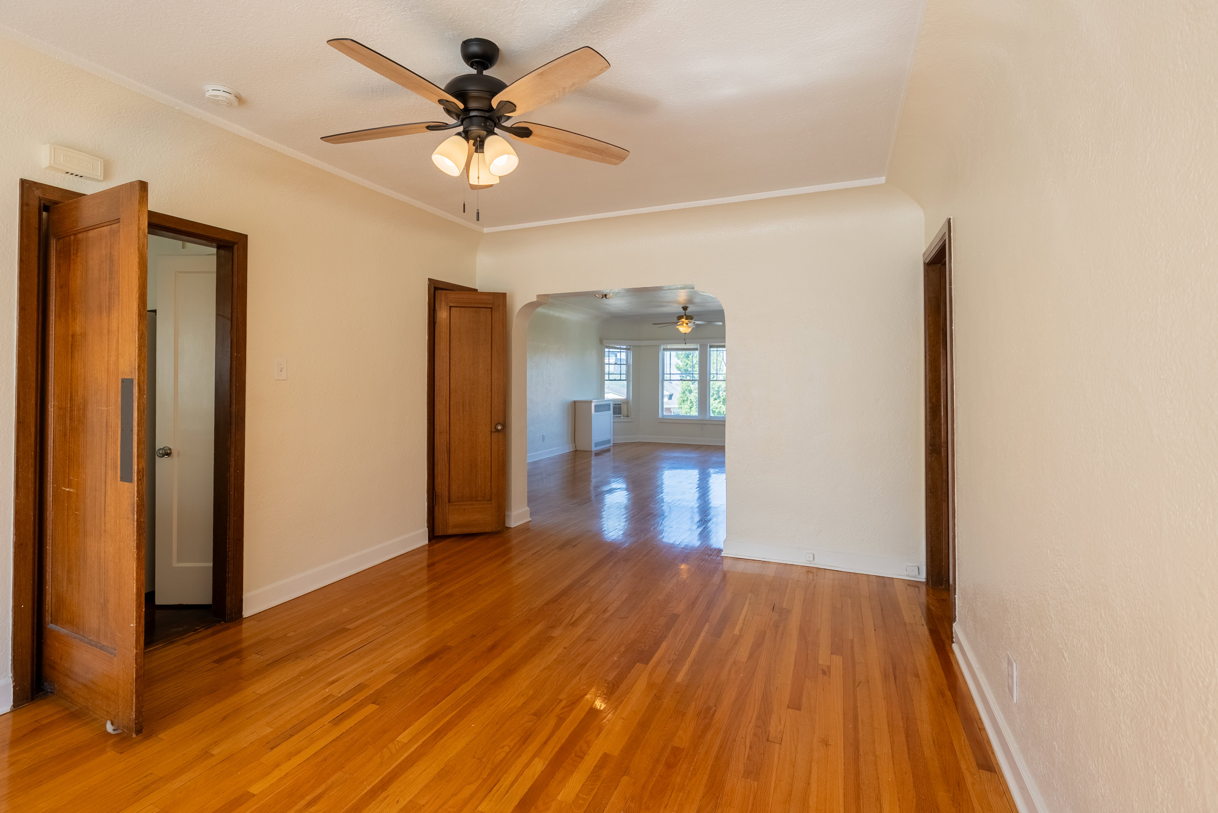 Hardwood flooring throughout, featuring a ceiling fan with integrated lighting, natural wood-finish doors, and an arched doorway