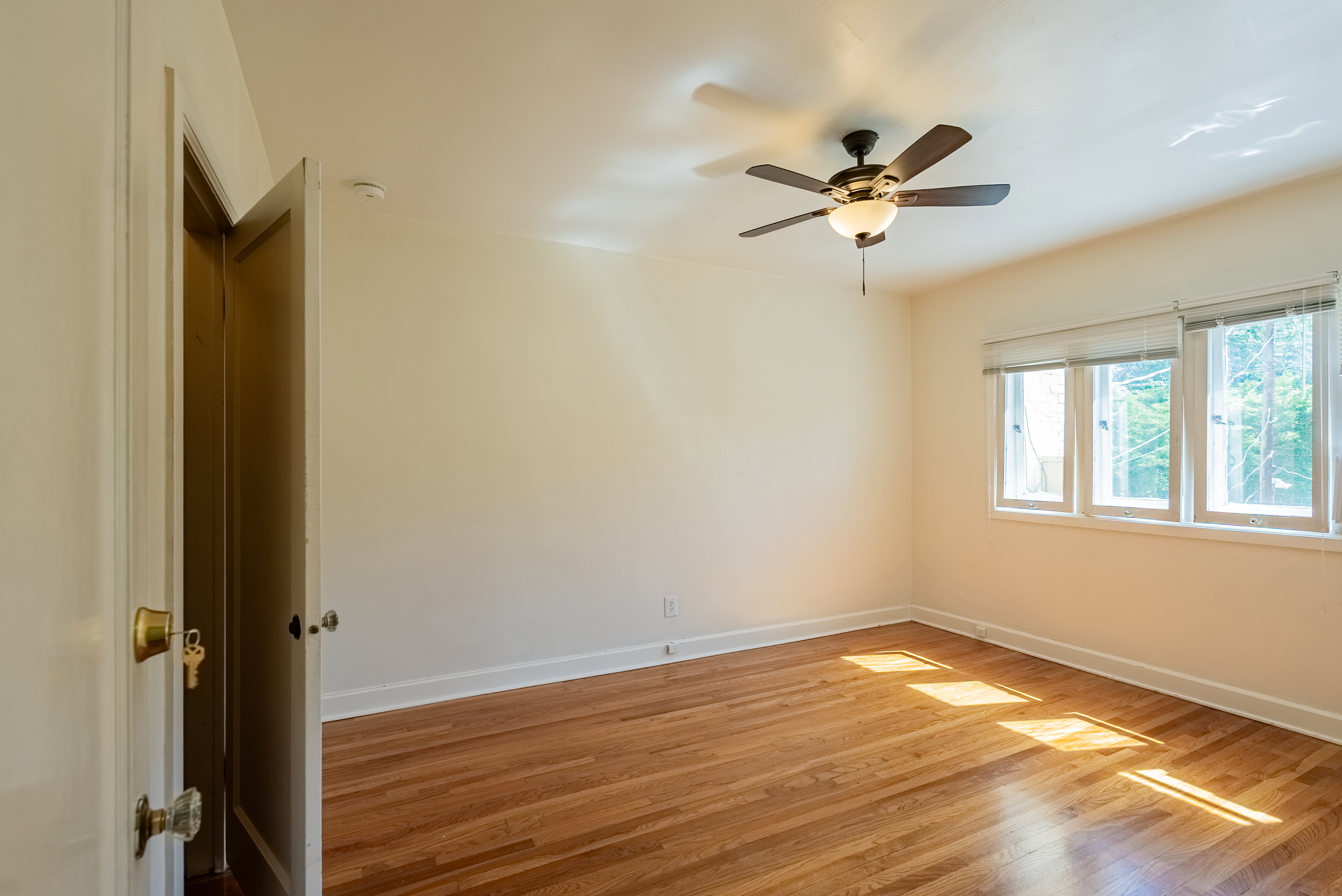 Spacious room featuring wood-finish flooring, white walls, and a ceiling fan with integrated lighting