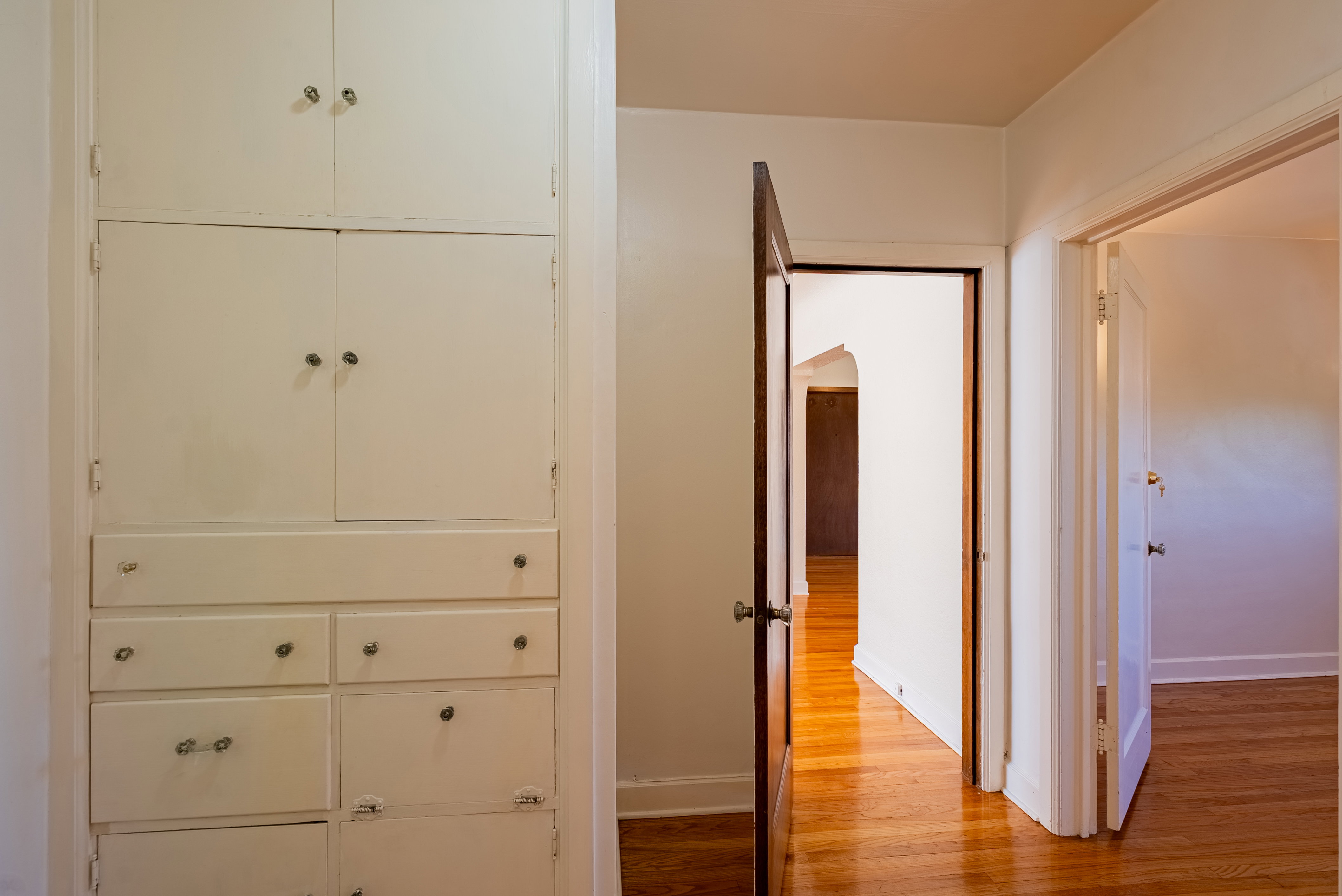 Built-in storage cabinetry featuring multiple drawers and upper cabinets, accompanied by wood-finish flooring extending into interior doorways