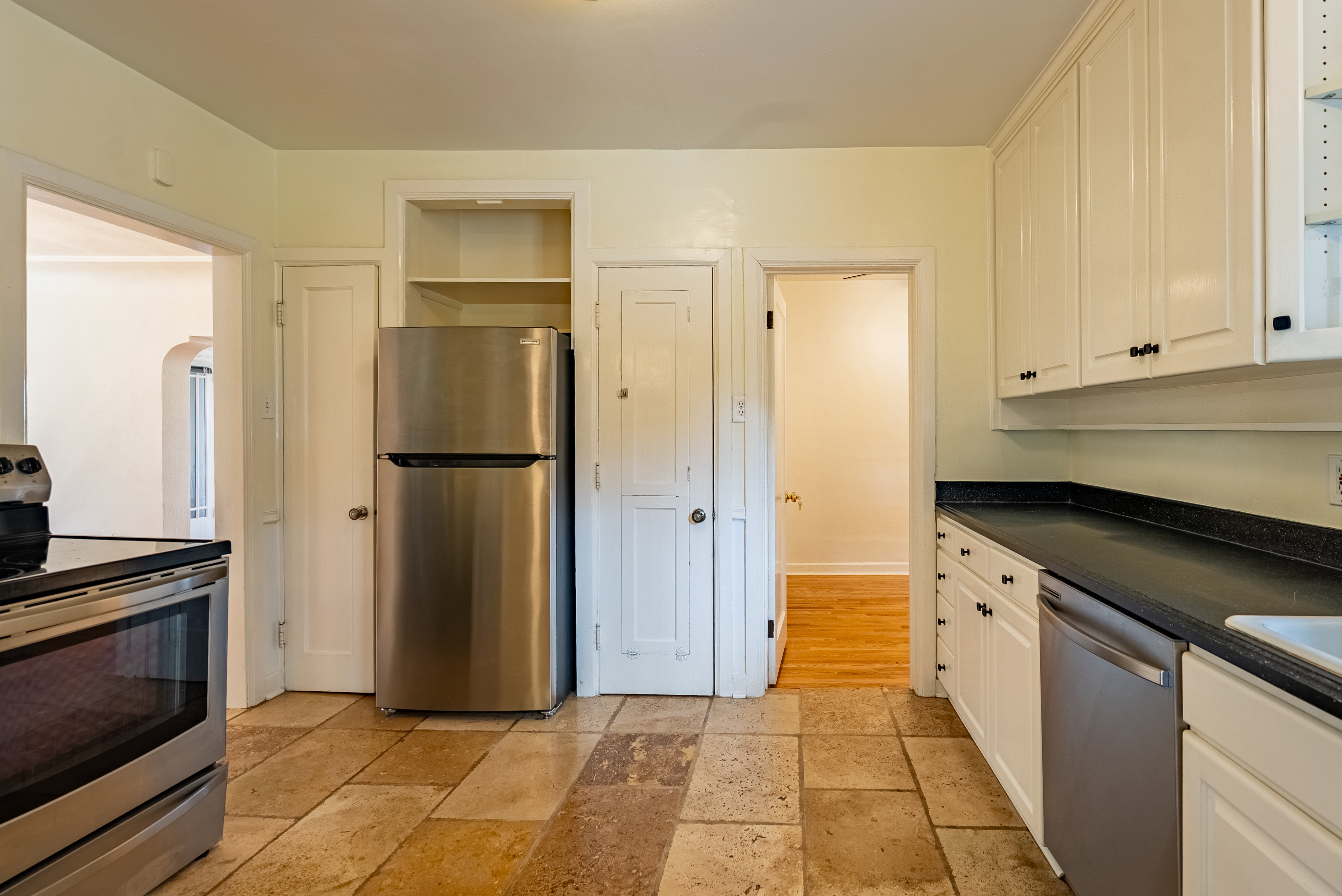 Kitchen featuring stone tile flooring, white cabinetry with black hardware, stainless steel appliances, and dark countertops