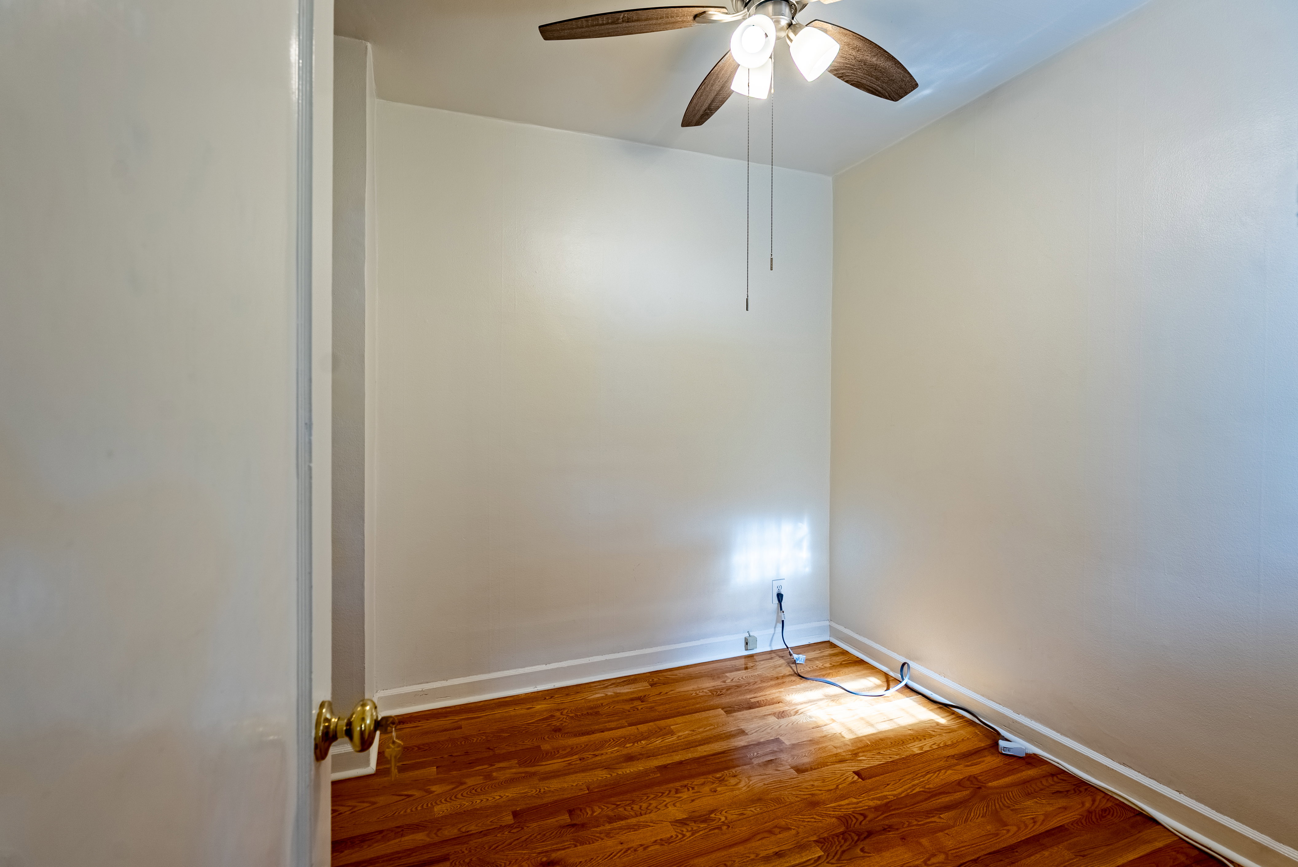 Neutral-toned room featuring wood-finish flooring, white baseboards, and a ceiling fan with integrated lighting