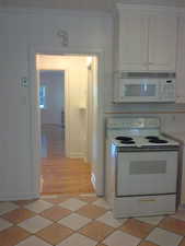 Apt #2 > Kitchen with white appliances, white cabinetry, crown molding, and light countertops