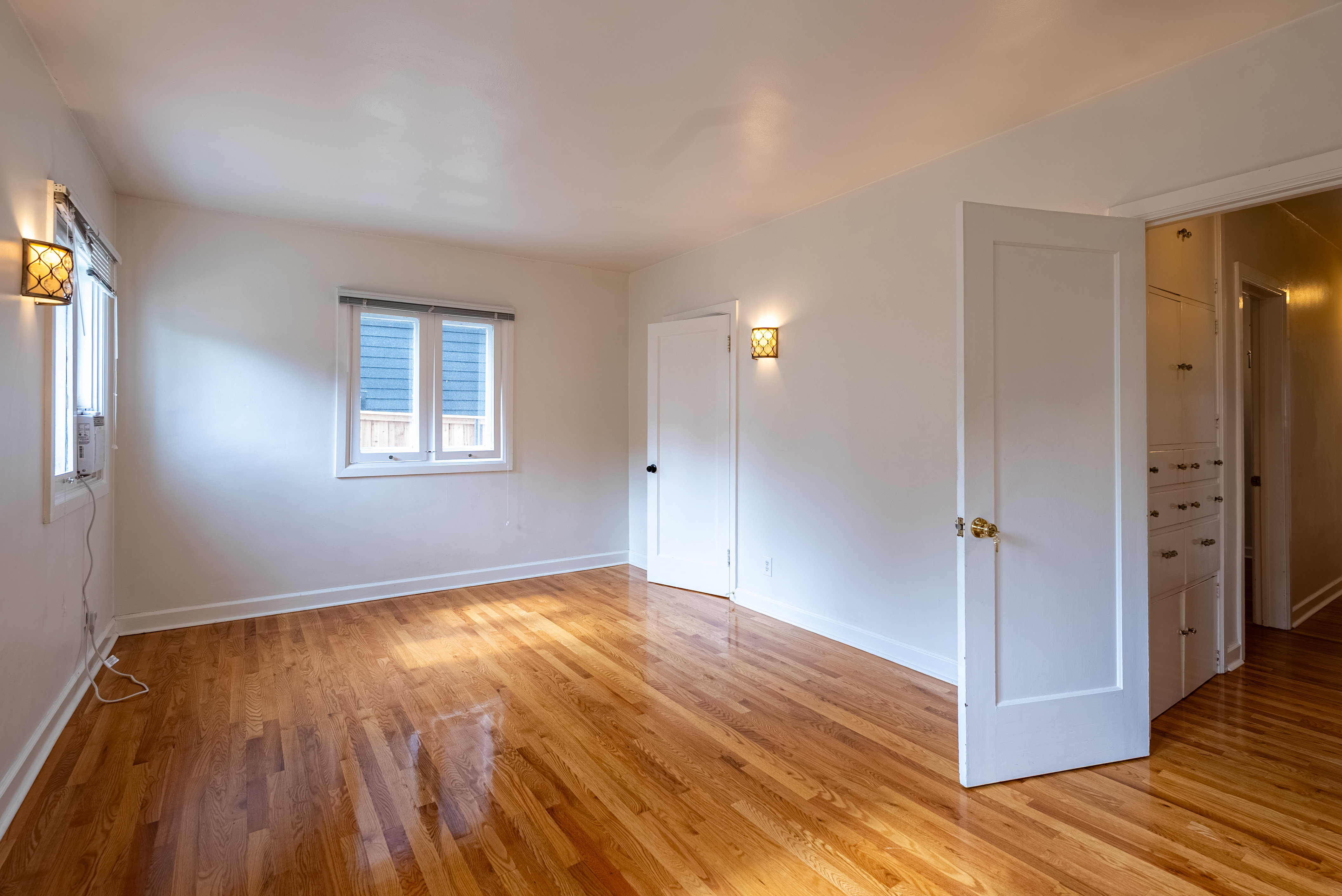 Bright room featuring wood-finish flooring, white walls, and two windows with white trim