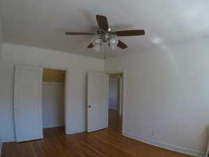 Apt # 8 > Unfurnished bedroom with dark wood-type flooring, a ceiling fan, crown molding, and a walk in closet