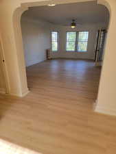 Apt # 9 > Empty room featuring arched walkways, a ceiling fan, light wood-style floors, and radiator
