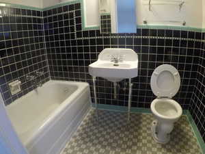 Apt # 4 >  Full bathroom featuring tile walls, dark tile patterned floors, shower / washtub combination, and a wainscoted wall