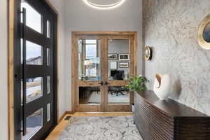 Entryway featuring wood finished floors, wallpapered walls, an accent wall, and french doors