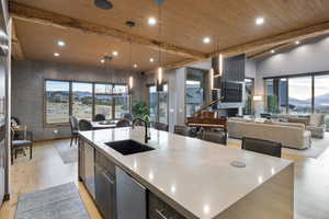 Kitchen with open floor plan, a large island, modern cabinets, a wood ceiling with exposed beams, and decorative light fixtures