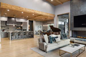 Living room featuring a wooden ceiling with exposed beams, an accent wall, light wood-type flooring, recessed lighting, and a chandelier