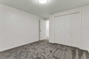 Unfurnished bedroom featuring dark colored carpet, a textured ceiling, and a closet
