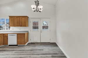 Kitchen with brown cabinets, vaulted ceiling, white dishwasher, light wood-style flooring, and light countertops