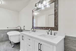 Full bath featuring tile walls, a wainscoted wall, double vanity, and a freestanding bath
