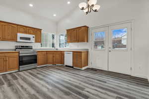 Kitchen featuring white appliances, brown cabinetry, dark wood finished floors, high vaulted ceiling, and a chandelier