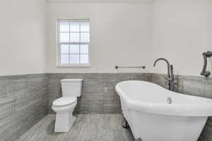 Full bath featuring tile walls, wainscoting, and a soaking tub