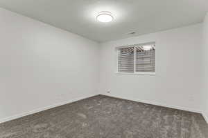 Unfurnished room featuring a textured ceiling and dark carpet