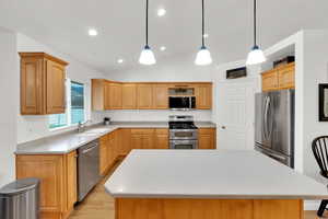 Kitchen with appliances with stainless steel finishes, a kitchen island, vaulted ceiling, and LVP flooring