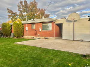 Back of house featuring brick siding, a lawn, and a patio area