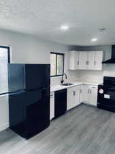 Kitchen with black appliances, light countertops, white cabinets, light wood-type flooring, and a textured ceiling