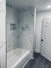 Bathroom with a combined bath / shower with marble appearance and dark wood finished floors