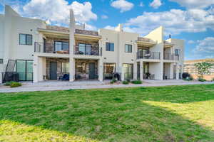 Rear view of property featuring a balcony, a lawn, stone siding, and a patio area