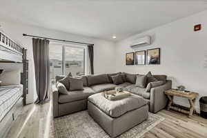 Living room featuring light wood-style flooring, a wall mounted AC, and a textured ceiling