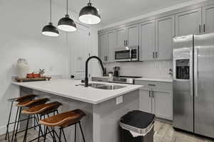 Kitchen featuring gray cabinets, stainless steel appliances, a peninsula, a breakfast bar, and pendant lighting
