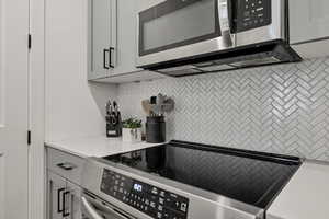 Kitchen with appliances with stainless steel finishes, gray cabinets, and decorative backsplash