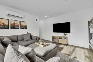 Living room featuring attic access, a wall unit AC, wood finished floors, and recessed lighting