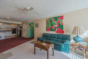 Living room with carpet, ceiling fan, and a textured ceiling