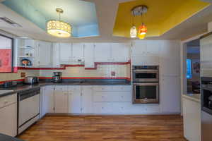 Kitchen with white cabinets, stainless steel appliances, light wood finished floors, a raised ceiling, and open shelves