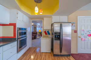 Kitchen featuring appliances with stainless steel finishes, pendant lighting, white cabinetry, and light wood-type flooring