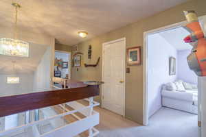 Corridor featuring a textured ceiling, a chandelier, an upstairs landing, and light colored carpet