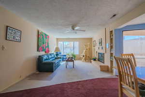 Living room featuring carpet floors, a textured ceiling, a ceiling fan, and a fireplace