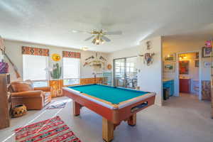 Primary bedroom used as rec room featuring pool table, a textured ceiling, wainscoting, light carpet, and a ceiling fan