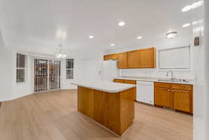 Kitchen featuring brown cabinetry, light countertops, a kitchen island, white appliances, and decorative light fixtures
