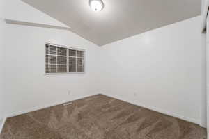 Carpeted empty room featuring vaulted ceiling and baseboards