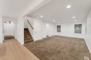 Basement with arched walkways, recessed lighting, stairs, light wood-style floors, and light colored carpet