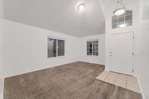 Foyer with light colored carpet, high vaulted ceiling, and light tile patterned floors