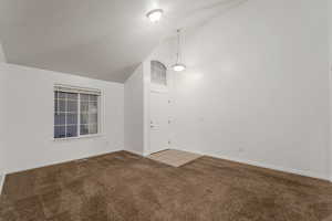 Carpeted empty room with high vaulted ceiling and baseboards