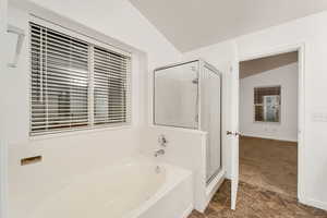 Full bathroom featuring vaulted ceiling, a garden tub, a shower stall, dark colored carpet, and dark stone finish flooring