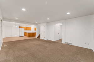 Unfurnished living room featuring recessed lighting, light colored carpet, arched walkways, stairs, and a chandelier