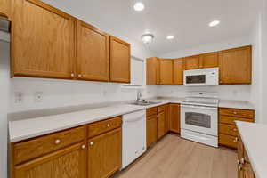Kitchen featuring white appliances, light countertops, recessed lighting, light wood finished floors, and brown cabinets
