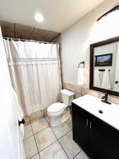 Full bath with curtained shower, vanity, tile walls, a wainscoted wall, and a textured ceiling