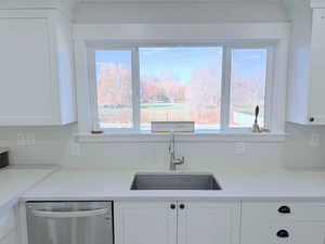 Kitchen with white cabinets, stainless steel dishwasher, and light stone countertops