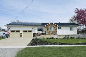 View of front of property featuring stone siding, concrete driveway, solar panels, a front lawn, and a garage