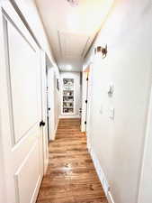 Hallway with light wood-style flooring, built in features, and attic access