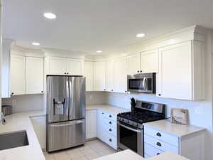 Kitchen featuring stainless steel appliances, white cabinetry, light stone counters, light tile patterned floors, and recessed lighting
