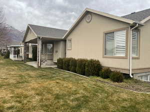 View of side of property featuring a yard, stucco siding, a porch, and roof with shingles