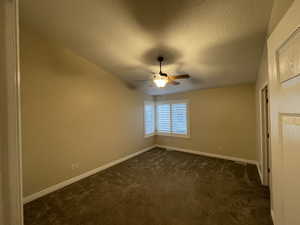 Unfurnished room featuring a textured ceiling, dark colored carpet, and a ceiling fan